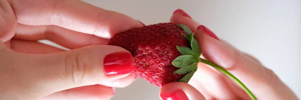 Close-up of female hand with red varnish manicure holding luscious ripe strawberry. Healthy eating and diet concept