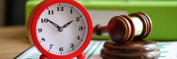 Close-up of judges gavel with alarm clock on financial documents. Postponement of a hearing, trial or auction end time. Court time and deadline concept