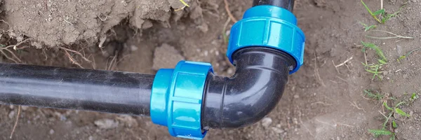 Close-up of elbow fitting and pvc pipes at bend in dirt trench outdoors. Plumbing water drainage installation. Underground irrigation system concept