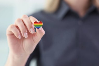 Kadının elinde LGBT gökkuşağı bayrağı renginde küçük bir kalp rozeti var. Kadın temsilcilere saygı ve destek gösteriyor