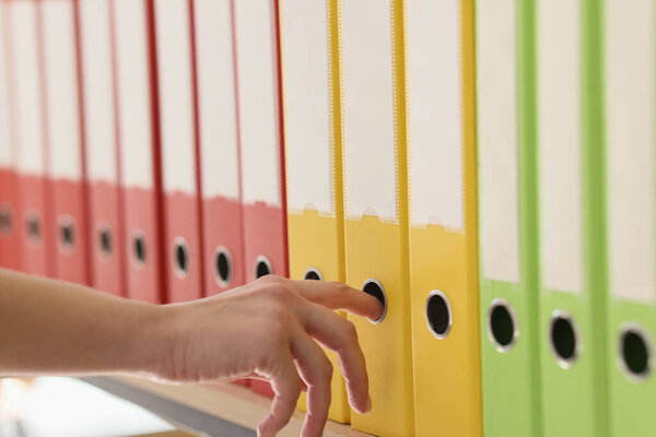 Organized ring binder structure and office files with data. Hand of woman taking yellow folder with accounting documents from archive row