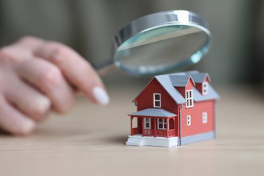 Ahşap masa yüzeyinde duran iki katlı evin modelinin üstünde büyüteç tutan bir kadın eli. Mülk inşa kavramının denetlenmesi