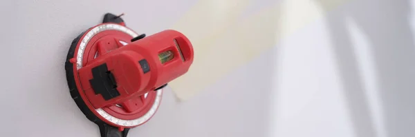 Close-up of red construction laser level fixed on white wall. Professional measuring device for marks. Renovation concept