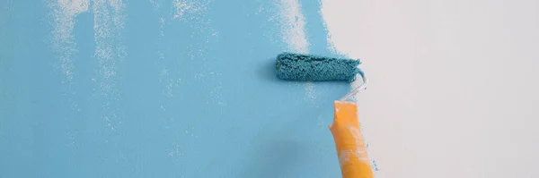 Close-up of professional decorator painting wall in blue color. Painting walls with roller. Repair and renovation concept