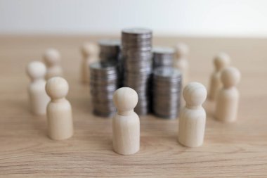 Tahta masadaki beyaz insan figürleriyle çevrili gümüş paralar. İnsanlar büyük gelir beklentisiyle kârlı bir iş projesi üzerinde çalışıyorlar.