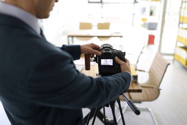 Adam modern ofiste boş bir masanın fotoğrafını çekmek için profesyonel kamerayı tripoda yerleştiriyor. Takım elbiseli bir erkek, iş yerinde nesneleri yakalıyor.
