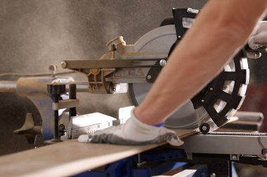 Koruyucu eldivenli adam tahta testeresi ile çalışıyor. Profesyonel, ev onarımı için malzemelerin işlenmesinde modern ekipman kullanıyor