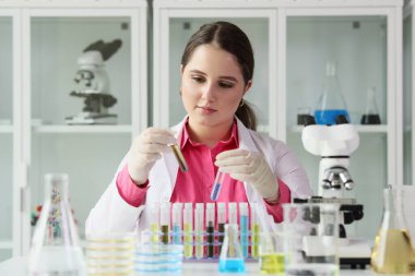 Genç bayan laboratuvar teknisyeni, mikroskop ve matarayla masada oturan sıvılarla test tüplerini inceliyor. Kimyager madde örneklerini inceler.