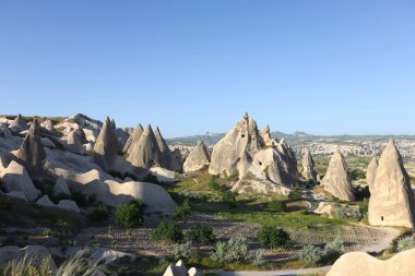 Yeşil çayırlı volkanik manzara. Mavi gökyüzünün altında koni şeklinde kayalar olan dağlık bir manzara. Kapadokya Türkiye 'de doğal kökenli popüler turizm beldesi
