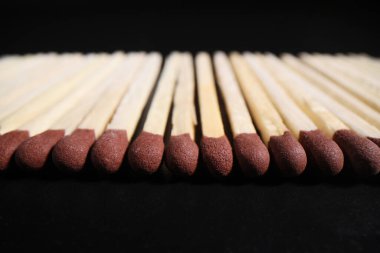 Kahverengi başlı kibritler uzun bir sıra halinde ışıklandırılmaya hazır. Koyu arkaplanda ateş yakmak ya da yemek pişirmek için tahta kibrit çöpleri