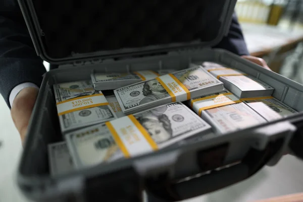 Manager holds open case with counted stacks of dollar banknotes in hands. Man shows briefcase with money paid for successful deal by client