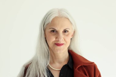 Uzun gri saçlı çekici yaşlı kadın açık arkaplanda poz veriyor. Stüdyoda seksi gülüşü olan olgun bir kadın model. Olumlu yaşlı bayan.
