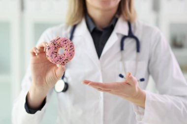 Laboratuvar önlüklü beslenme uzmanı elinde pembe kremayla taze çörek tutuyor. Kadınlar tatlı tatlının sağlık ve vücut ağırlığı üzerindeki etkilerinden bahseder.
