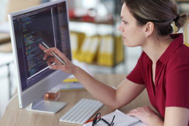 Akıllı kadın kalemi bilgisayar ekranına çeviren program kodlarını kontrol ediyor. Programcı, ofisindeki tahta masada oturan monitöre bakıyor.