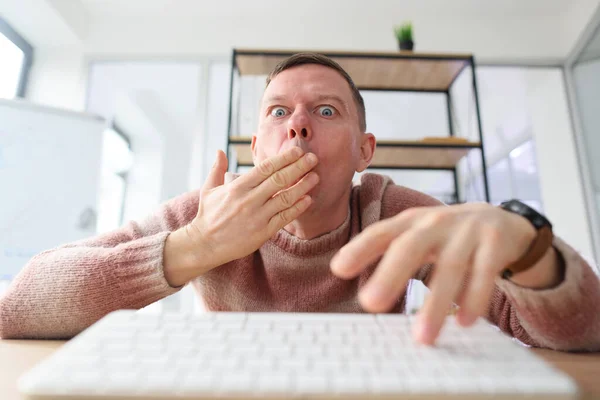 衝撃的な男はキーボードを入力しながら手のひらを開いて目を広く口をカバーします 従業員はウェブサイトの統計情報を見て驚きます — ストック写真