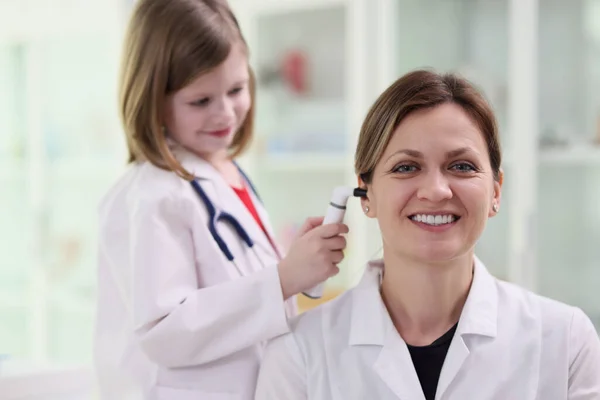 穿着医疗制服的可爱小女孩用快乐女人的耳镜检查耳朵 好奇的孩子在医生的职业梦想中学习做健康检查 — 图库照片