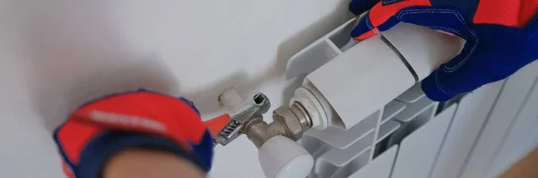 Close-up of male plumber installing heating radiator using pipe wrench. Builder installs new hot water central heating system using wrench. Renovation concept