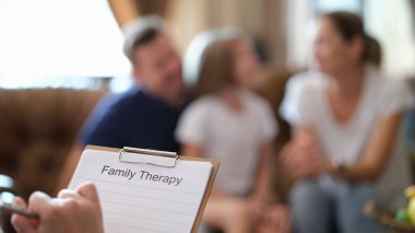 Psychologist ready to make notes listening to complaints of family. Specialist holds clipboard with blank paper against parents and kid on sofa clipart