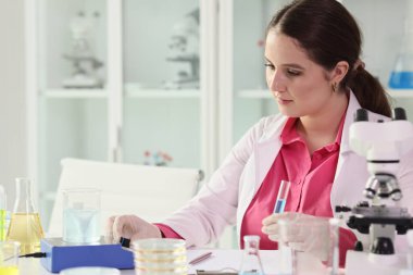 Odaklanmış esmer kadın elinde mavi sıvıyla test tüpü tutuyor. Kadın bilim adamı modern laboratuvarda ayırıcı hakkında detaylı araştırmalar yapıyor.