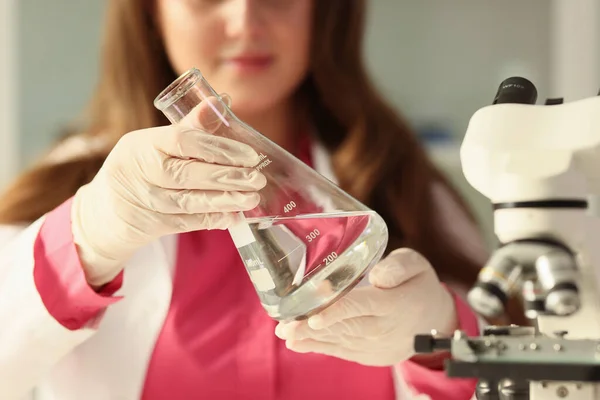 女子学生はきれいな水を手にガラスのフラスコを持っています ゴム手袋の焦点を当てた若い女性は 研究室で透明な液体を調べる — ストック写真
