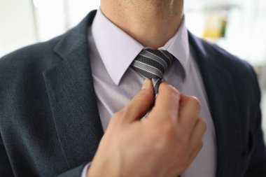 Başarılı iş adamı çizgili kravatı rahat hissetmek için eliyle düzeltir. Klasik takım elbiseli genç adam işte stresli hissediyor.