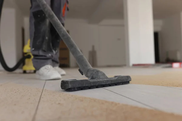 Foreman does industrial cleaning of laminate floor in room at process of renovation. Man vacuums sawdust from flooring with modern domestic appliance