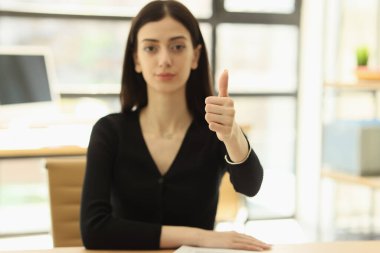 Siyah giysili esmer kadın kameraya bakıp parmağını kaldırıyor. Genç bayan çalışan şirket modern ofisinde çalışmayı onaylıyor