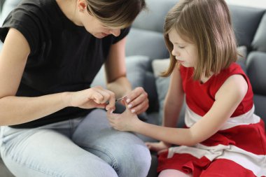 Bakıcı anne okuldan sonra kanepede oturan küçük kızın tırnaklarını kesiyor. Ebeveynler evde çocuk sağlığıyla ve hijyeniyle ilgilenirler.