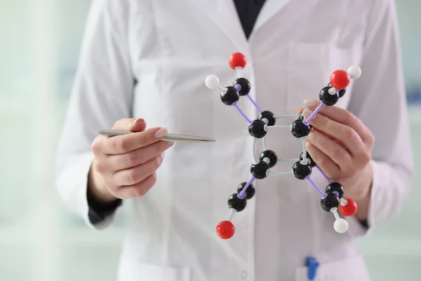 stock image Woman chemist in white lab coat points pen to molecule model holding in hand. Female scientist presents structure of atomistic system at seminar