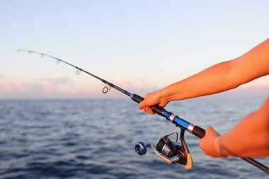 Close-up of woman sitting holding fish rod in hands. Female taking fish in sea or river. Fish and fishery concept clipart