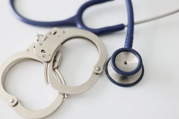 stock image Top view of metal handcuffs and stethoscope on white background. Medical crime, bribe and corruption concept