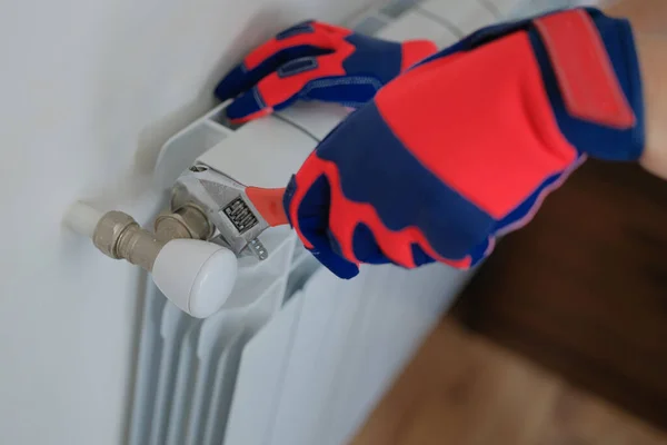 Close-up of male plumber hands in gloves installing or repairing heating radiator using wrench. Man builder installs new hot water central heating system using wrench