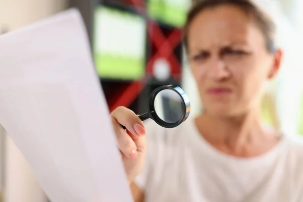 Portrait of woman trying read papers with magnifier glass, squinting to see more clearly. Female having difficulties seeing text because of vision problems