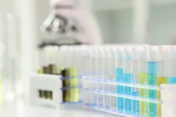カラフルな液体を持つ試験管のクローズアップ 背景に顕微鏡 ワクチンの開発 科学的調査 実験室試験の概念 — ストック写真