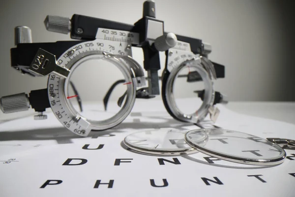 Modern optometric glasses for measuring visual acuity lie on paper Snellen chart. Medical device for checking eyesight waits for patient in clinic office