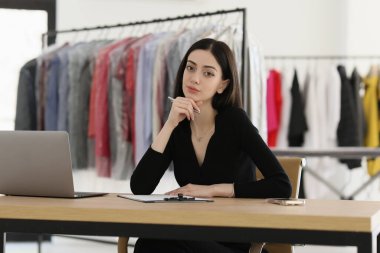 Kuru temizlemeciliğin düşünceli yöneticisi masa başında pano ve dizüstü bilgisayarla oturuyor. Kadın çalışan, temiz elbiseli askılı askılı çalışma görevlerini çözer