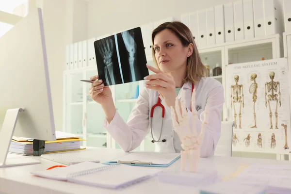 女医生研究病人手和胳膊坐在诊所办公桌前的X光照片 创伤学家控制伤后康复过程 — 图库照片