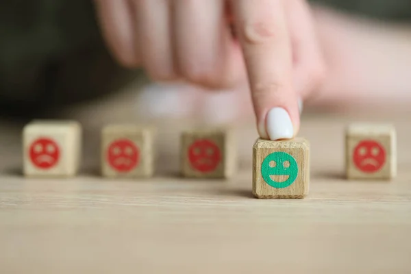 Change emotional state from negative to positive for wellbeing. Woman chooses wooden cube with green smiling face at table. Mental health