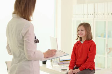 Dosyası olan kadın doktor hastane ofisinde randevusu sırasında küçük kızı muayene ediyor. Kadın pediyatrist hastayla röportaj yapıyor. Çocuklar için modern sağlık hizmeti
