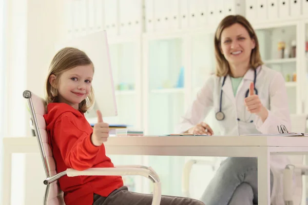 予約時に小さな女の子と女性の正医師が承認の親指の兆候を示しています 現代の病院で小児科の相談 子どもの健康支援 — ストック写真