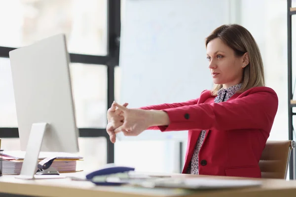 女性マネージャーはコンピュータの仕事を始める前に腕を伸ばす 真剣な女性でピンクのジャケット伸張中にブレーク座ってテーブルで光前提 — ストック写真