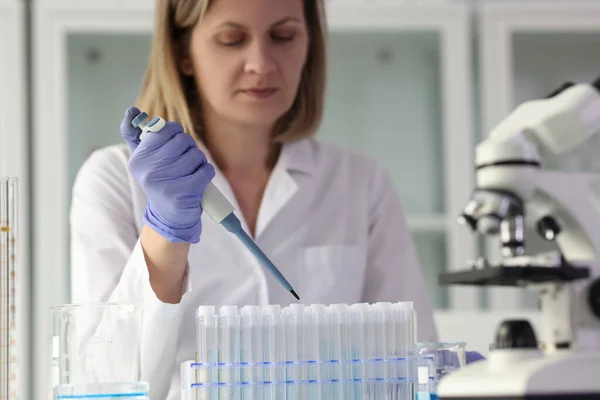 若い化学者は 液体物質のサンプルで設定された試験管にピペットで試薬を滴下します 研究室のコートの女性は研究室で科学的な研究を行います — ストック写真