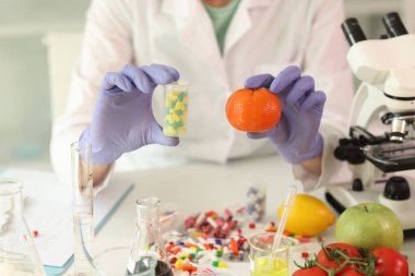 Masada elinde kapsüllü mandalina ve şişe tutan kadına karşı bir sürü hap var. Laboratuvardaki uyuşturucu ve organik ürünleri karşılaştıran tıbbi ve bilimsel araştırmalar