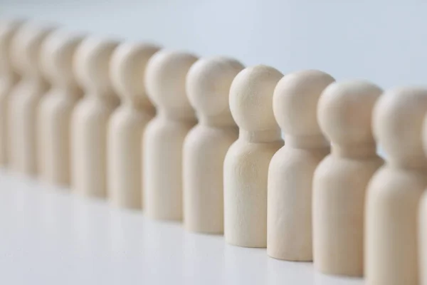 stock image Small wooden figures lined up in long row on white table. Discipline and strict control of employees at work in office. White figurines made of wood