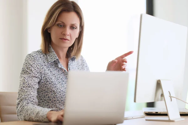 集中した女性はノートパソコンを見てコンピュータのモニターに指をポイントします 女性マネージャーは異なるウェブサイト上のデータと統計を比較します — ストック写真
