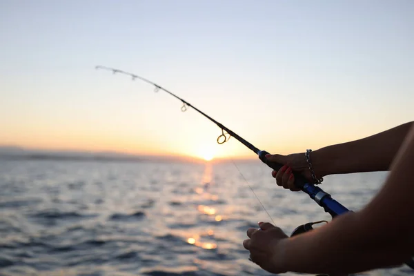 女人喜欢在日落时带着光波在海上航行的船上钓鱼 拿着长钓竿捕鱼的女人的手 — 图库照片