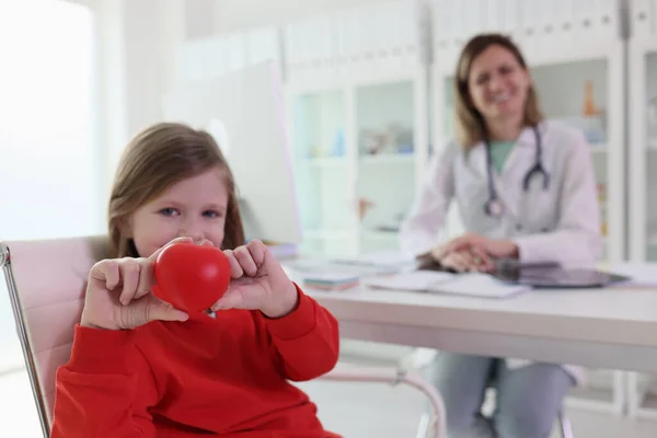 Menina Bonito Segura Brinquedo Coração Vermelho Mão Contra Médico Mesa — Fotografia de Stock