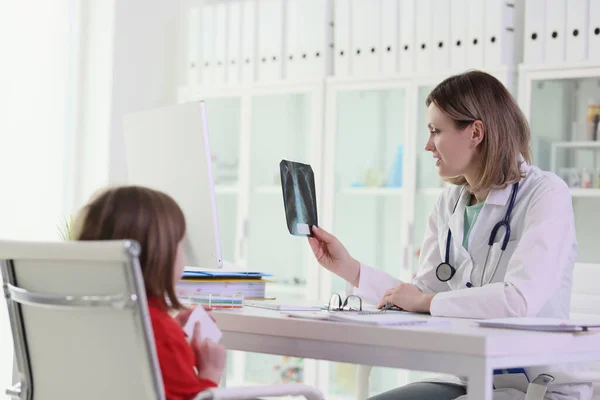 医生向坐在桌旁的小女孩展示了肺的X光图像 诊所里身着军服的妇女婴儿健康状况 — 图库照片