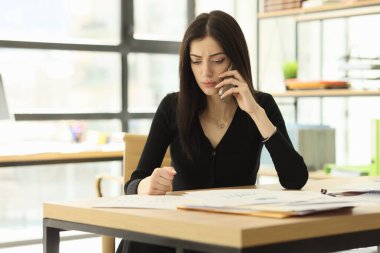 Ciddi sekreter telefonda müşteriyi dinliyor. İş yerindeki verileri karşılaştırıyor. Kadın çalışan şirket önerisinde ofis masasında oturarak sorunu çözmeye çalışıyor.