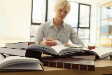 Kısa saçlı bir kadın, açık kütüphanedeki masada oturan kalın kitaplarda yüksek lisans işi arıyor. Kadın öğrenci kariyer gelişimi için bilgi topluyor